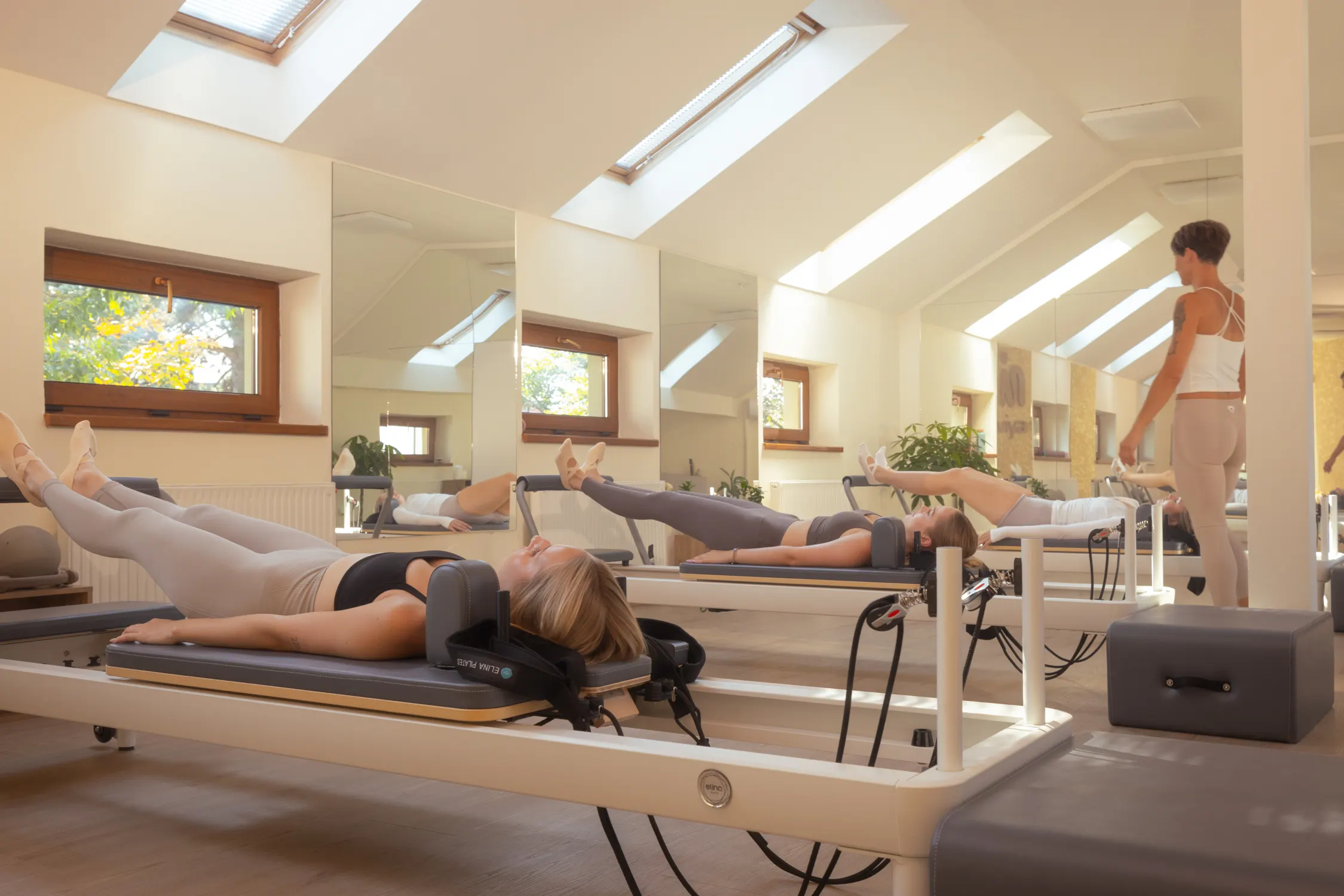 Klientky cvičící na strojích Pilates Reformer, v pozadí lektorka