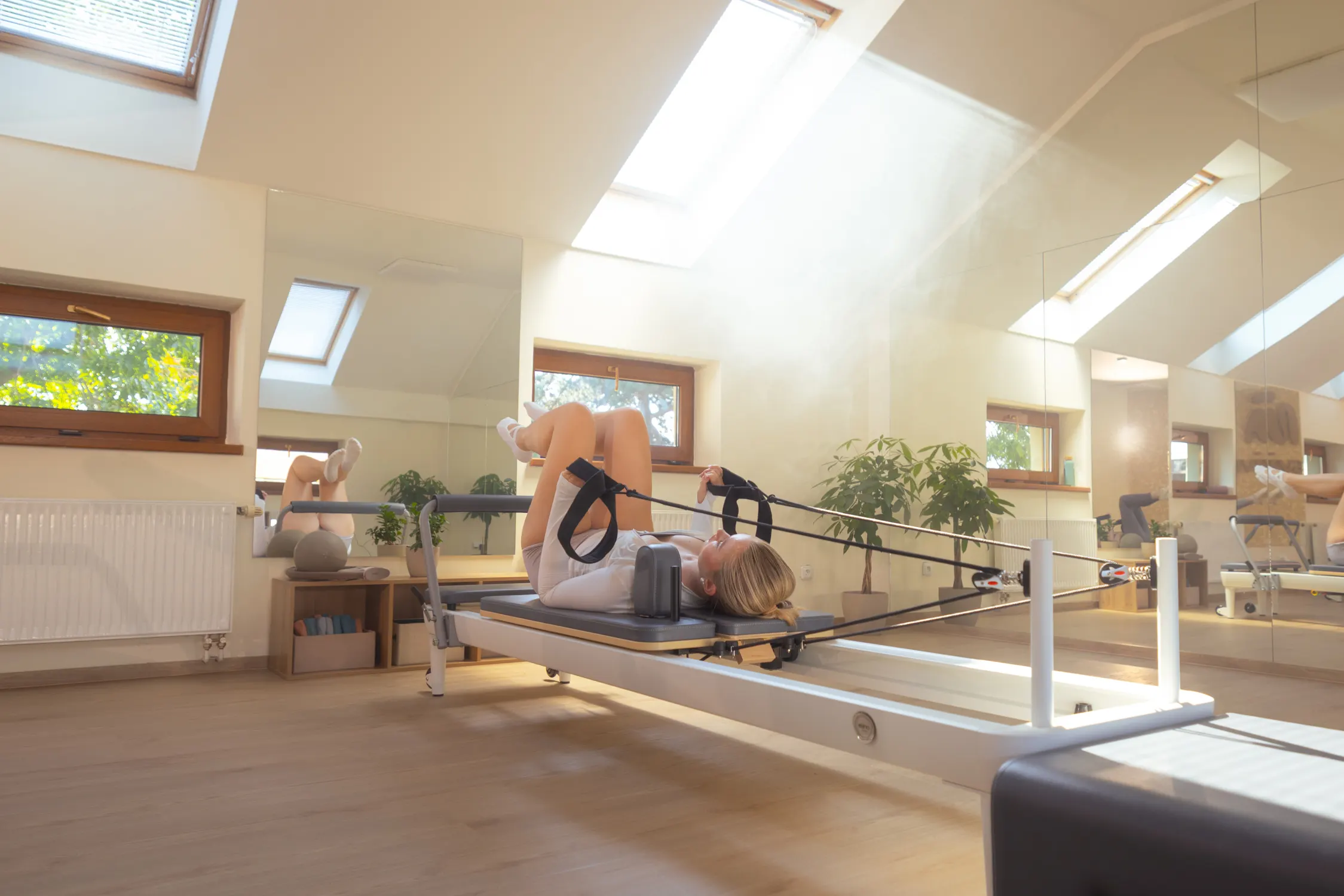 Klientka při cvičení na stroji Pilates Reformer, prosvětlený prostor